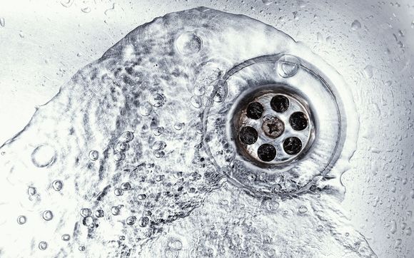 Water flows down a drain in a metal sink.