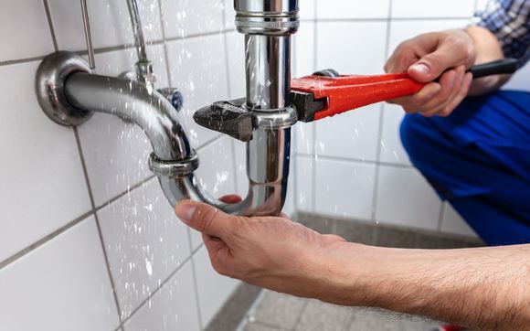 Plumber fixing a leaky pipe with a wrench in a bathroom. Water spraying.
