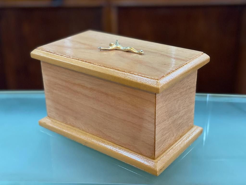 Una caja de madera con una cruz encima está sobre una mesa de vidrio.