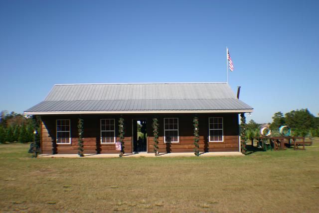 Brown wooden building with windows and American flag on a grassy field under a blue sky.