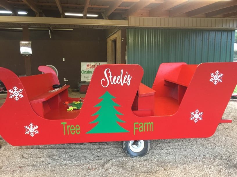 Red sleigh on wheels, Steele's Tree Farm.  Green tree graphic, white snowflakes,  under awning with green and brown wall.