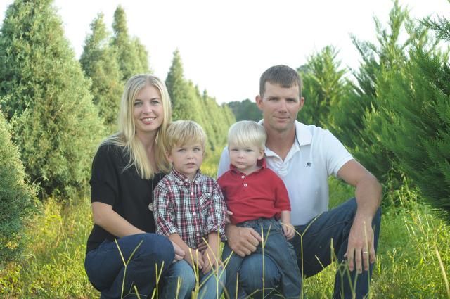 Family of four kneeling in a field of evergreen trees; mother and father with two young children.