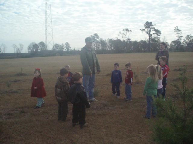 A group of children and adults standing in a field, possibly planting trees.