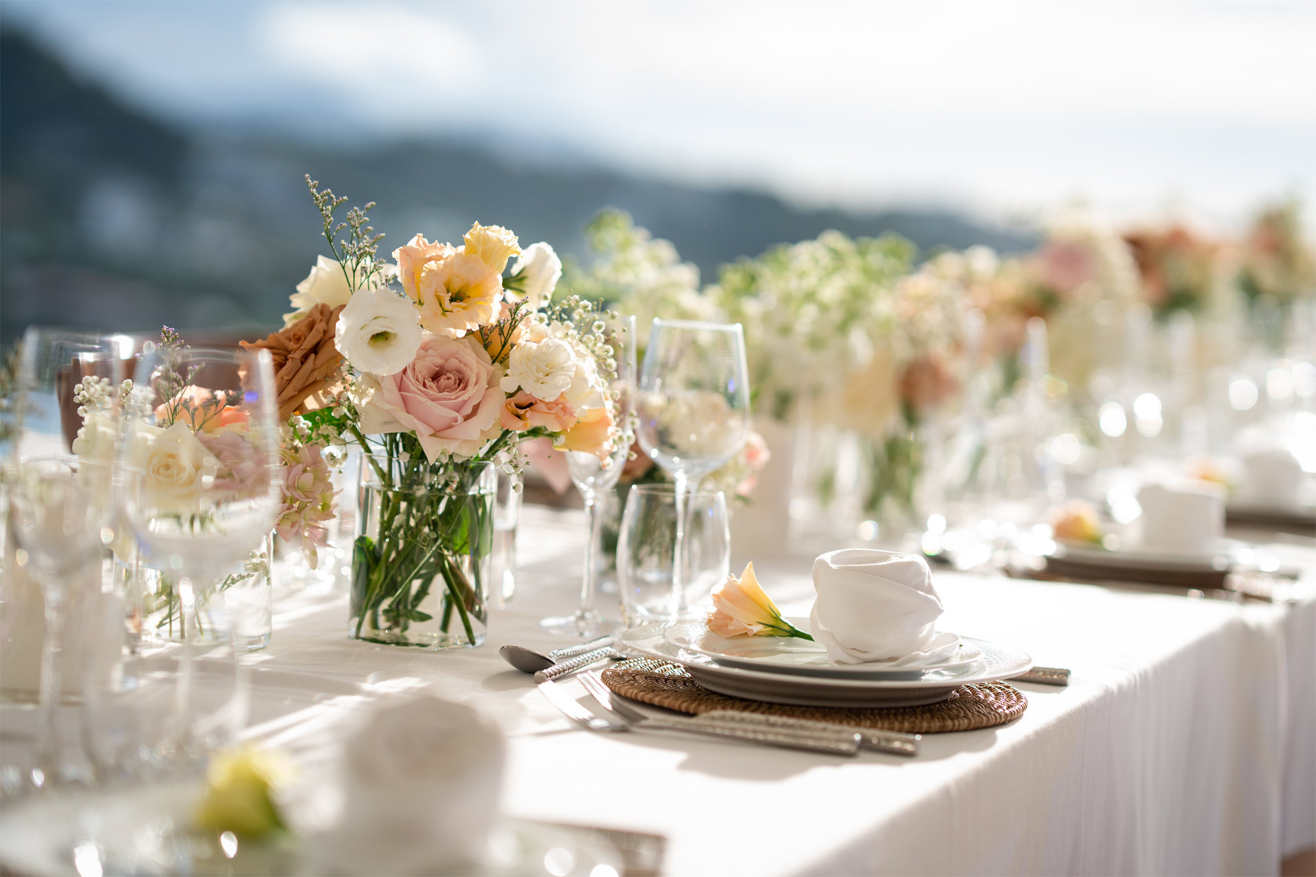 A long table with plates , glasses , and flowers on it.