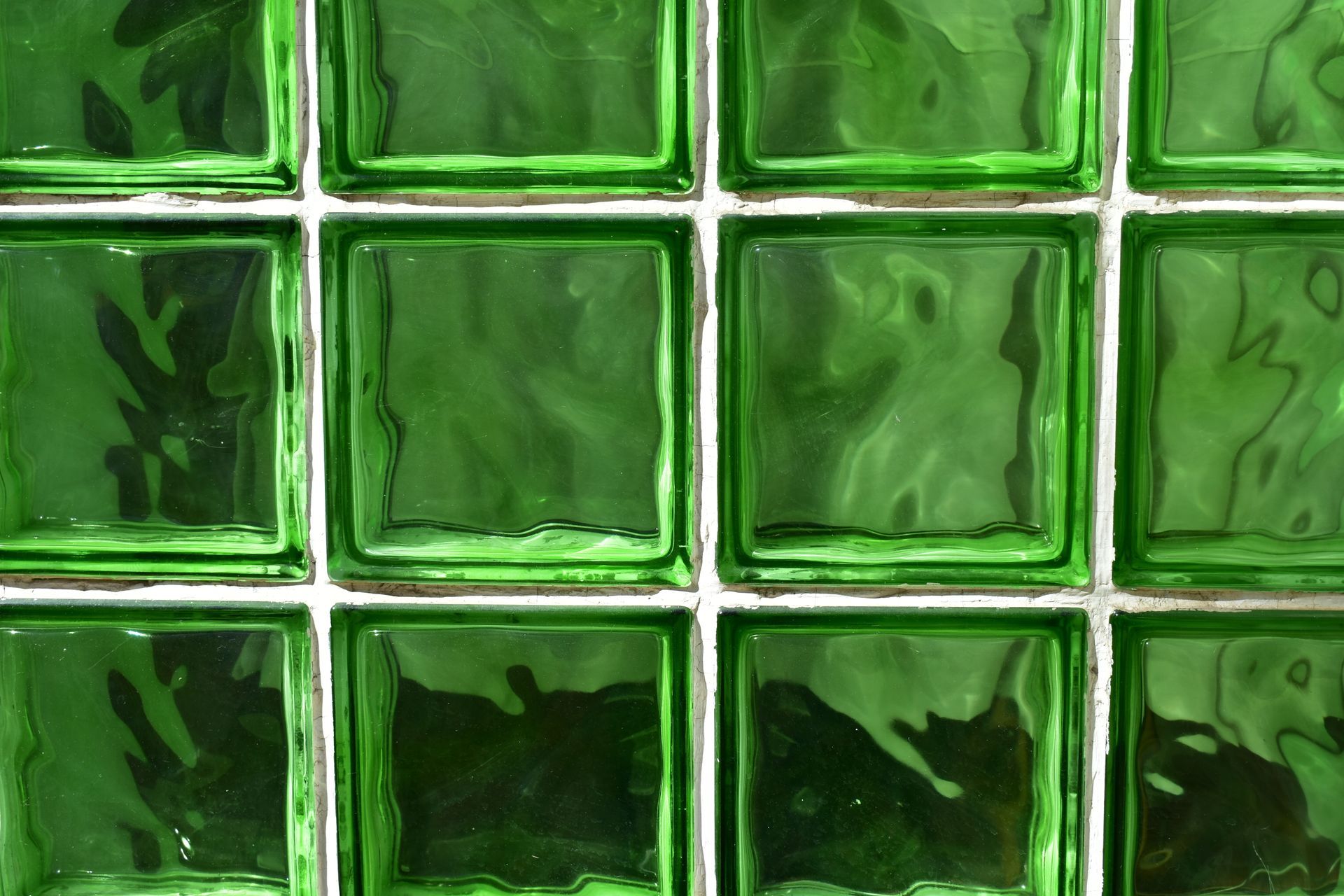 A grid of square, green-tinted textured glass blocks set within white mortar joints. A grid of square, green-tinted textured glass blocks set within white mortar joints.