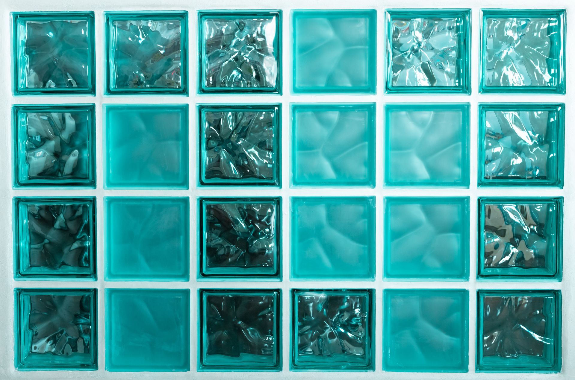 A grid of teal glass blocks, showing a mix of smooth and textured surfaces. A grid of teal glass blocks, showing a mix of smooth and textured surfaces.