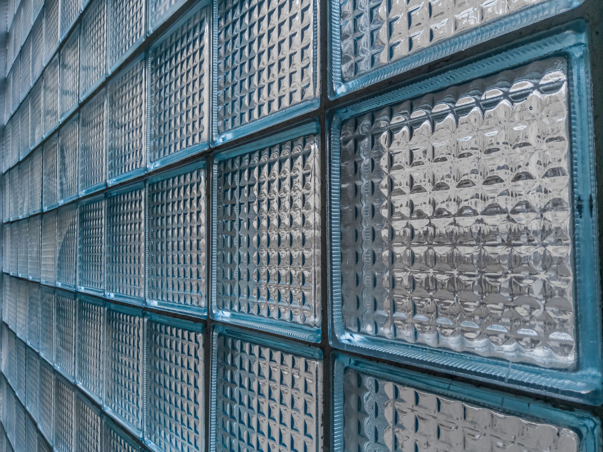A close-up, angled view of a textured glass block wall with a repetitive grid pattern, illuminated by natural light. A close-up, angled view of a textured glass block wall with a repetitive grid pattern, illuminated by natural light.