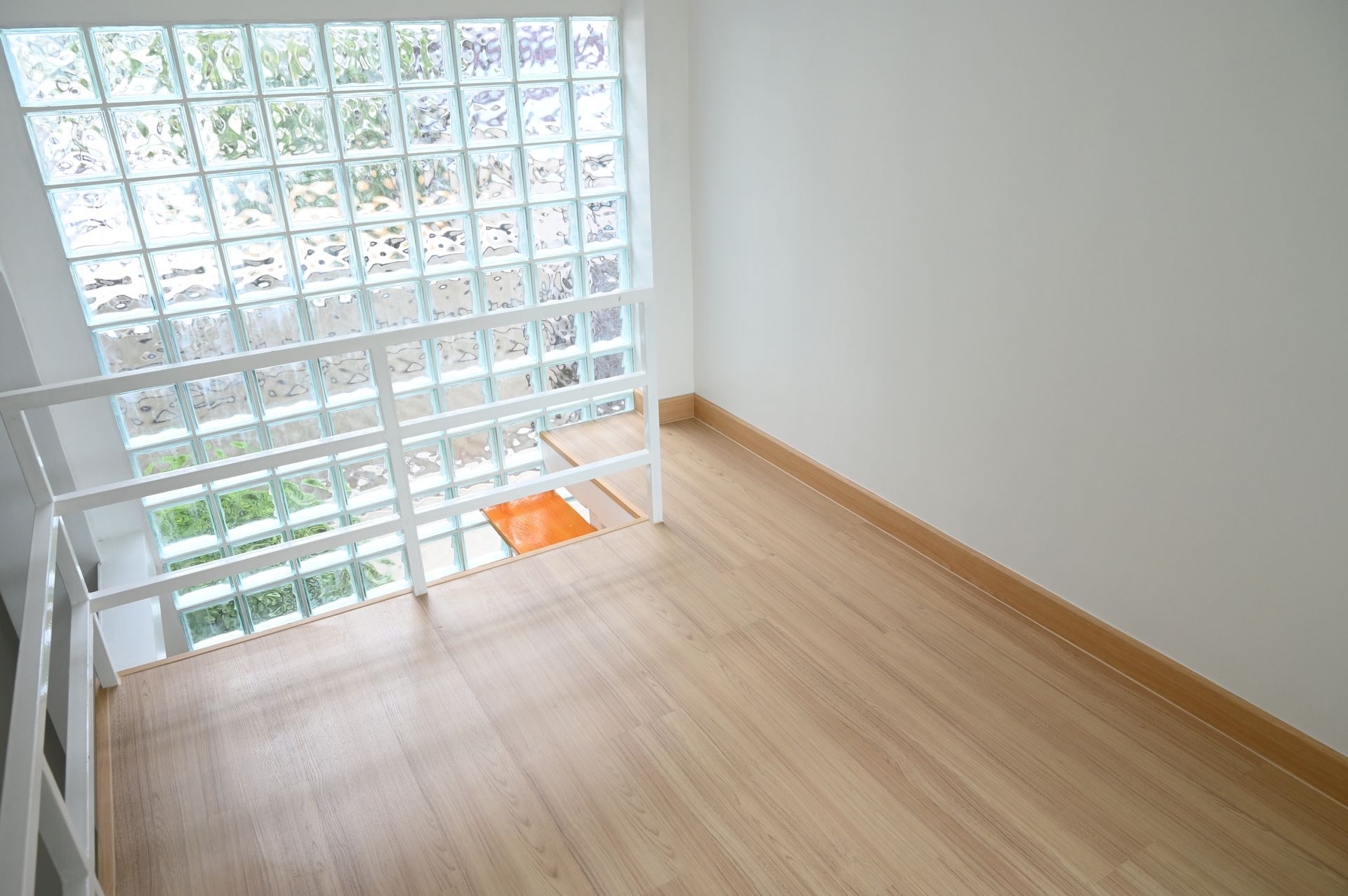 A bright room featuring light wood flooring, a white wall, and a large grid of glass blocks against a white railing. A bright room featuring light wood flooring, a white wall, and a large grid of glass blocks against a white railing.