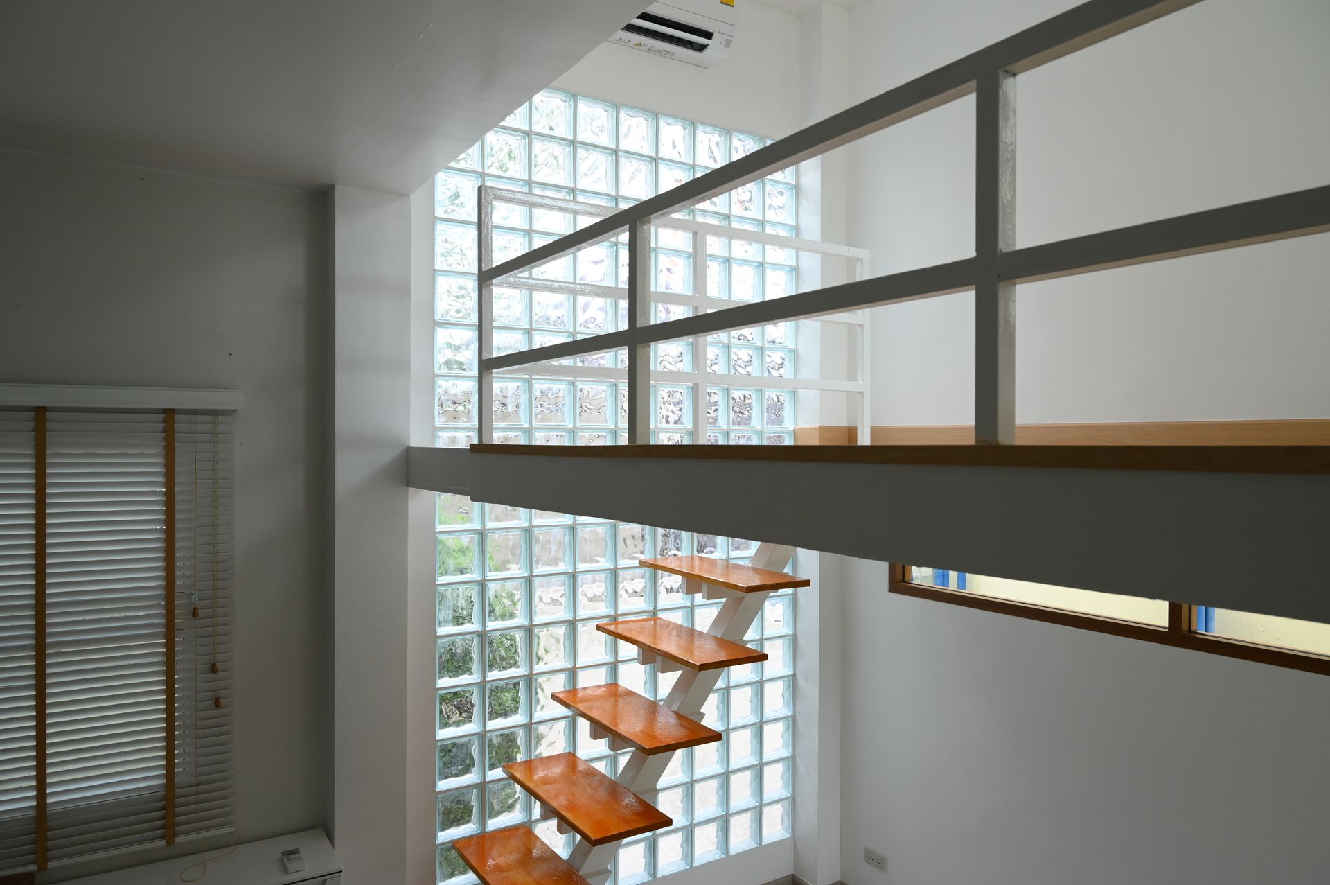Modern interior with a floating wooden staircase, a loft level with a metal railing, and a tall glass block feature wall.