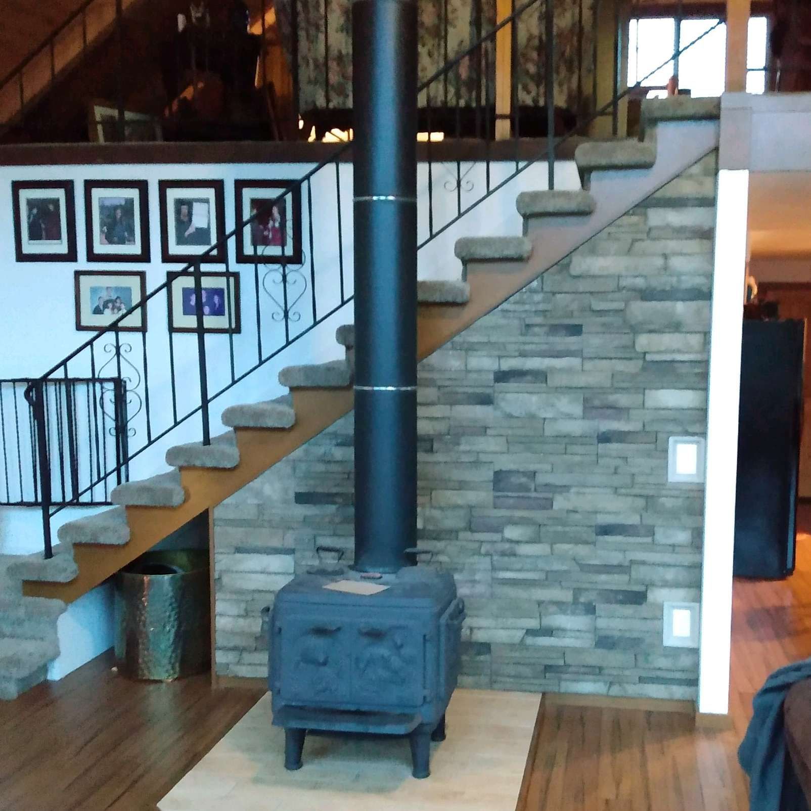 A wood stove sits under a staircase in a living room