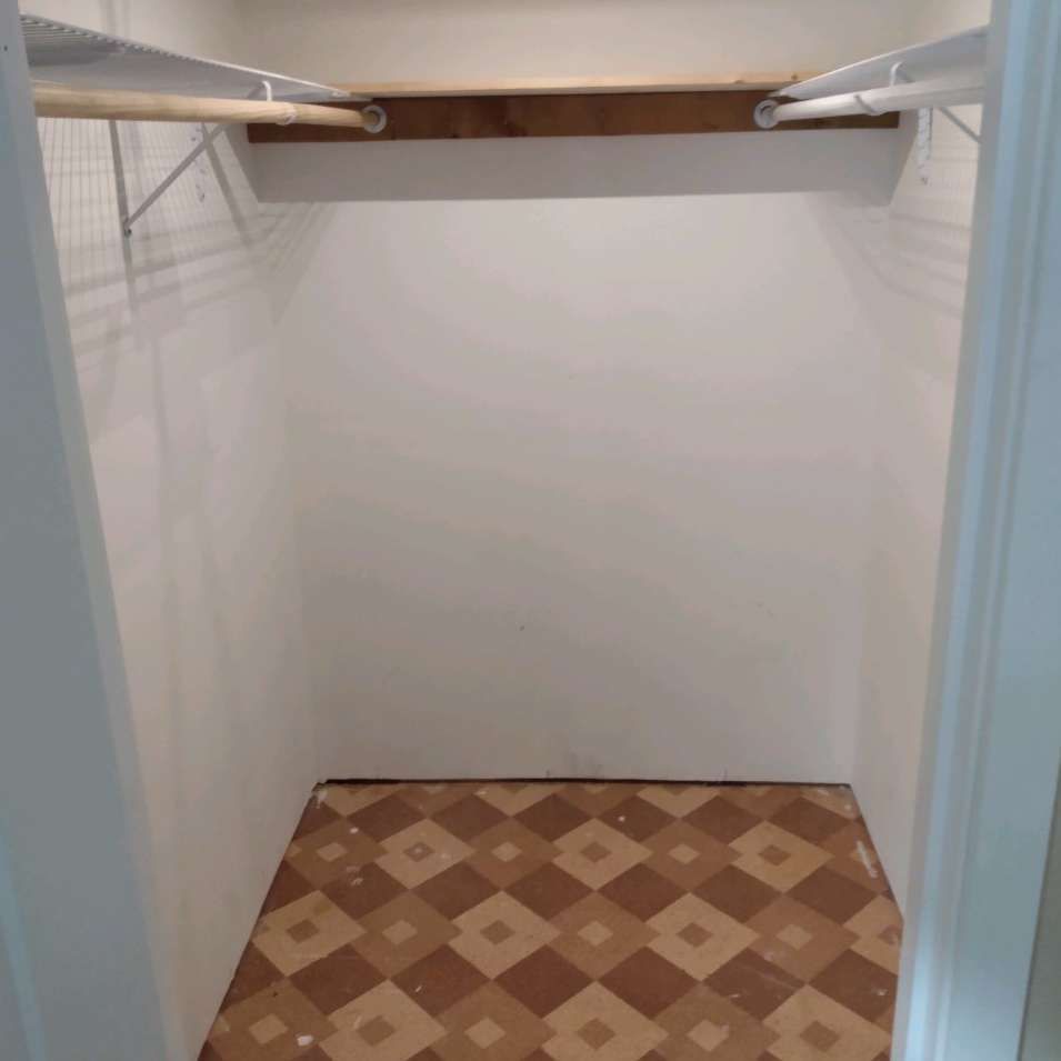 An empty closet with a wooden floor and white walls.