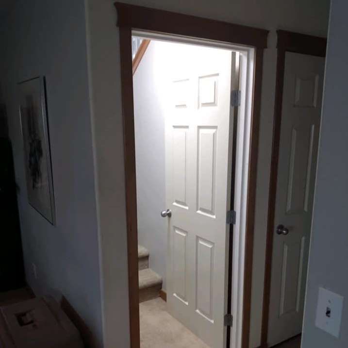 A hallway with a white door and stairs in the background.
