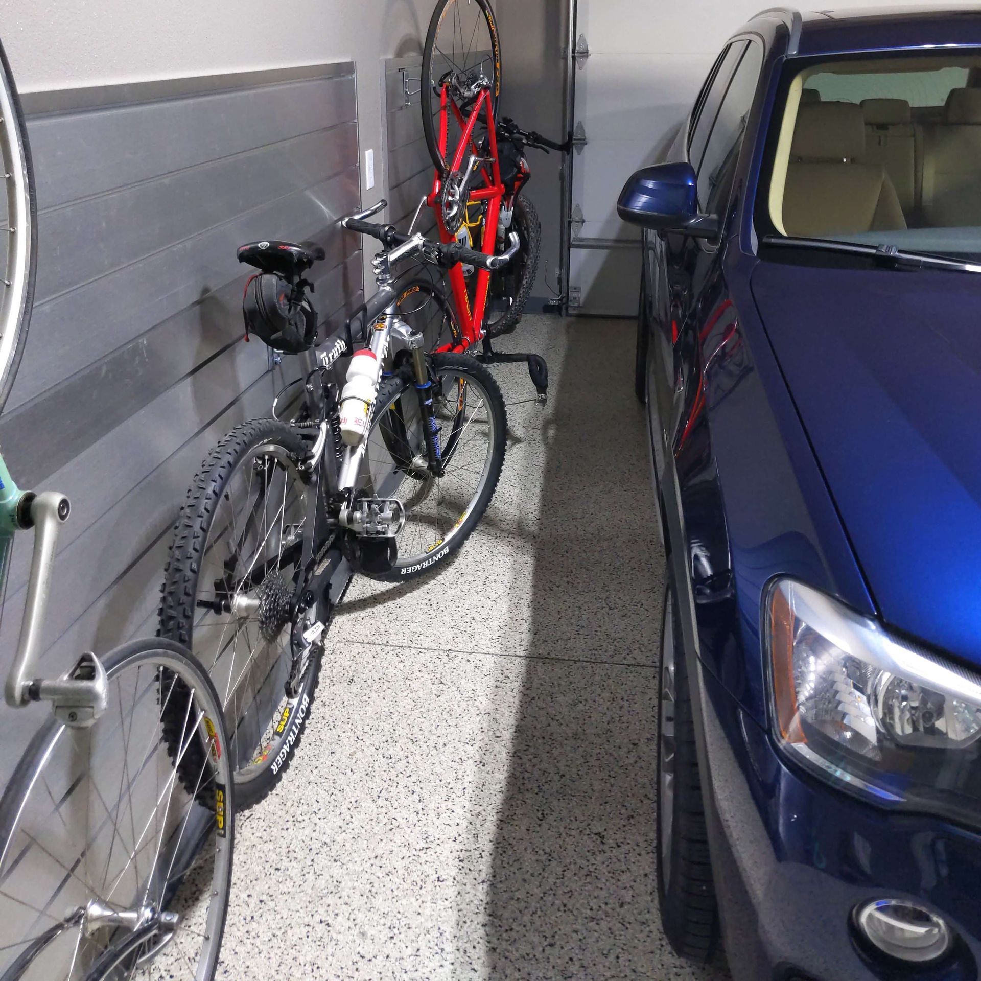 A blue car is parked in a garage next to bicycles