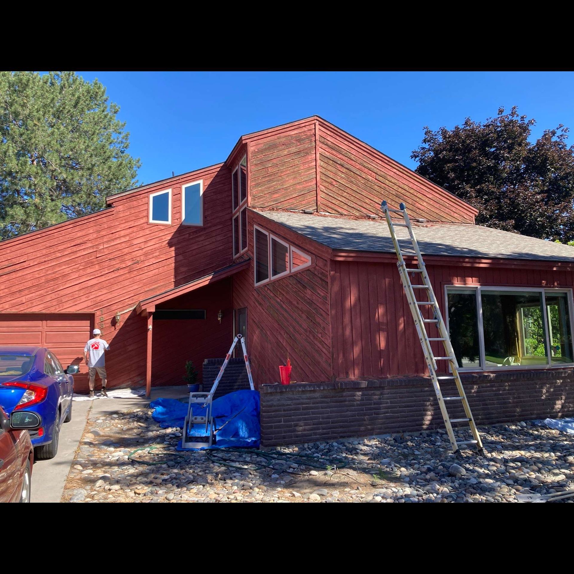 A man is standing in front of a red house with a ladder.