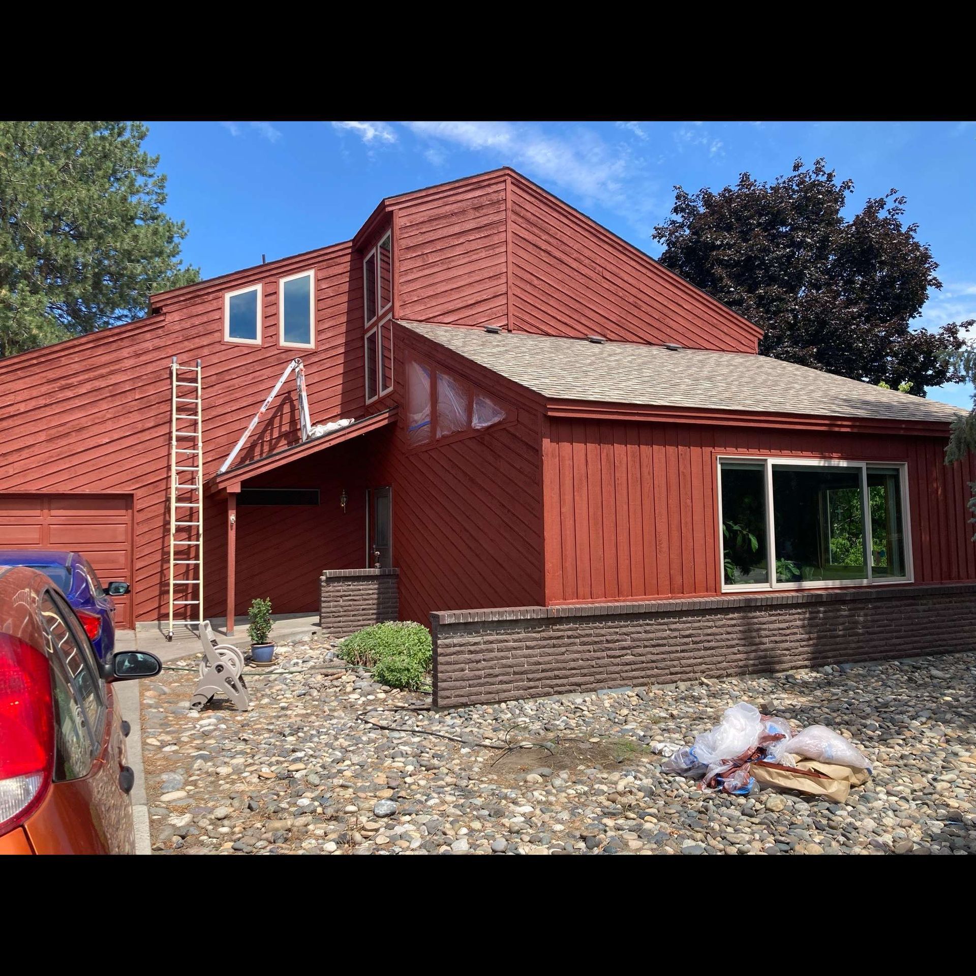 A red house with a ladder on the side of it and a car parked in front of it.