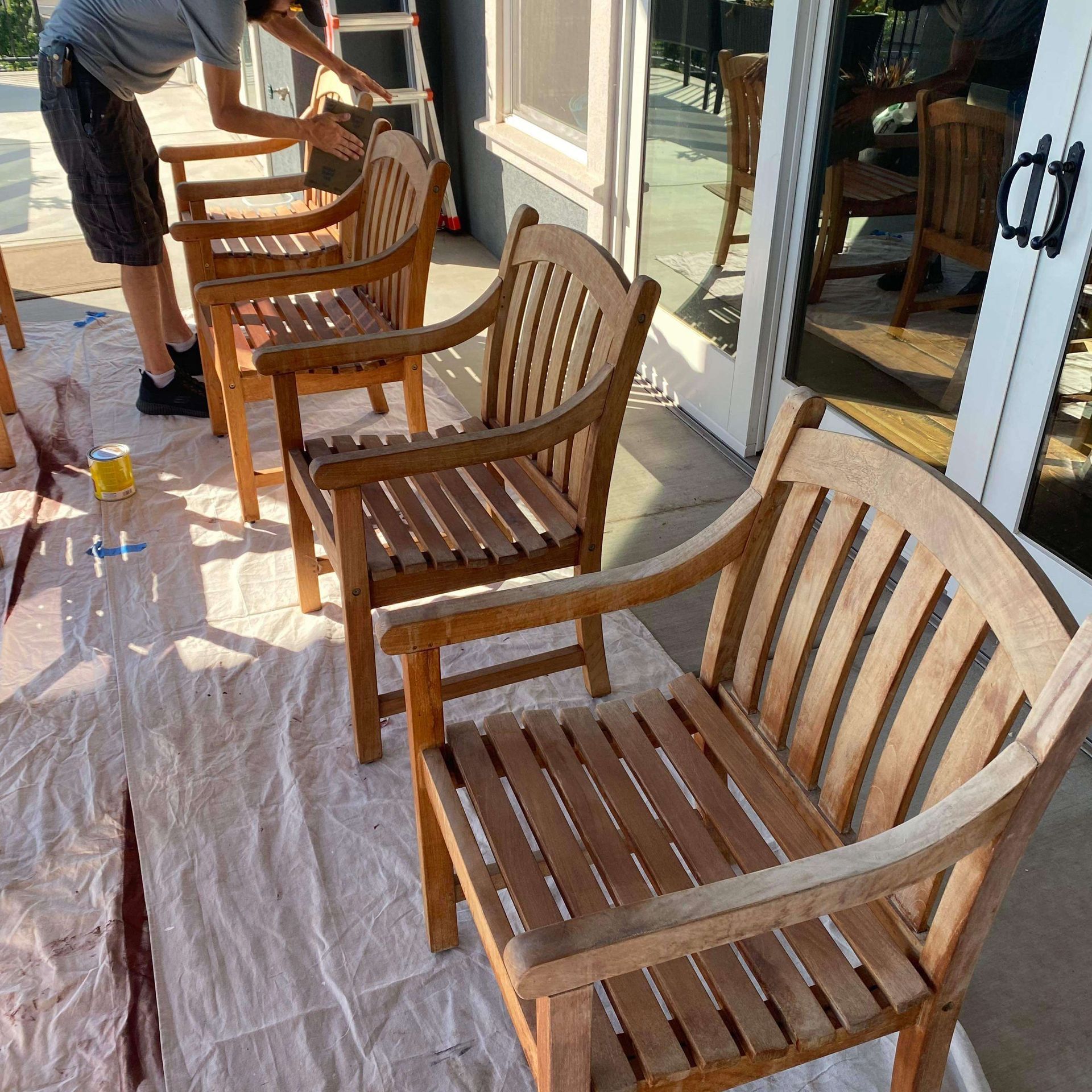 A man is painting a row of wooden chairs