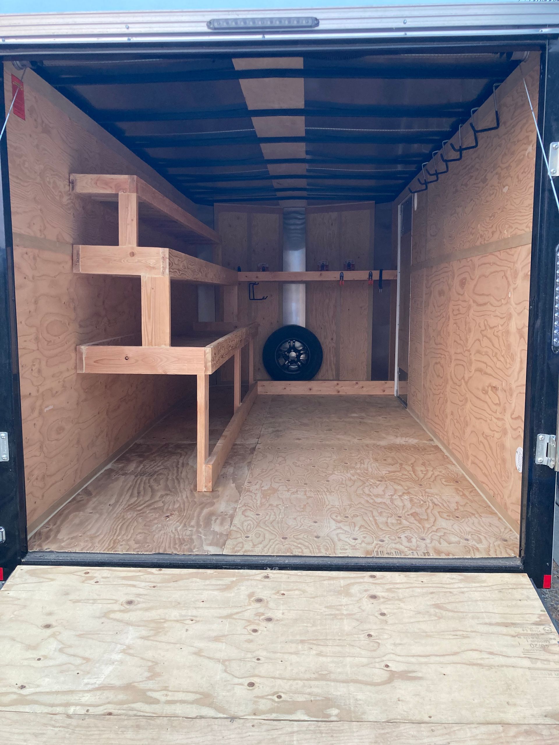 The inside of a trailer with shelves and a tire.