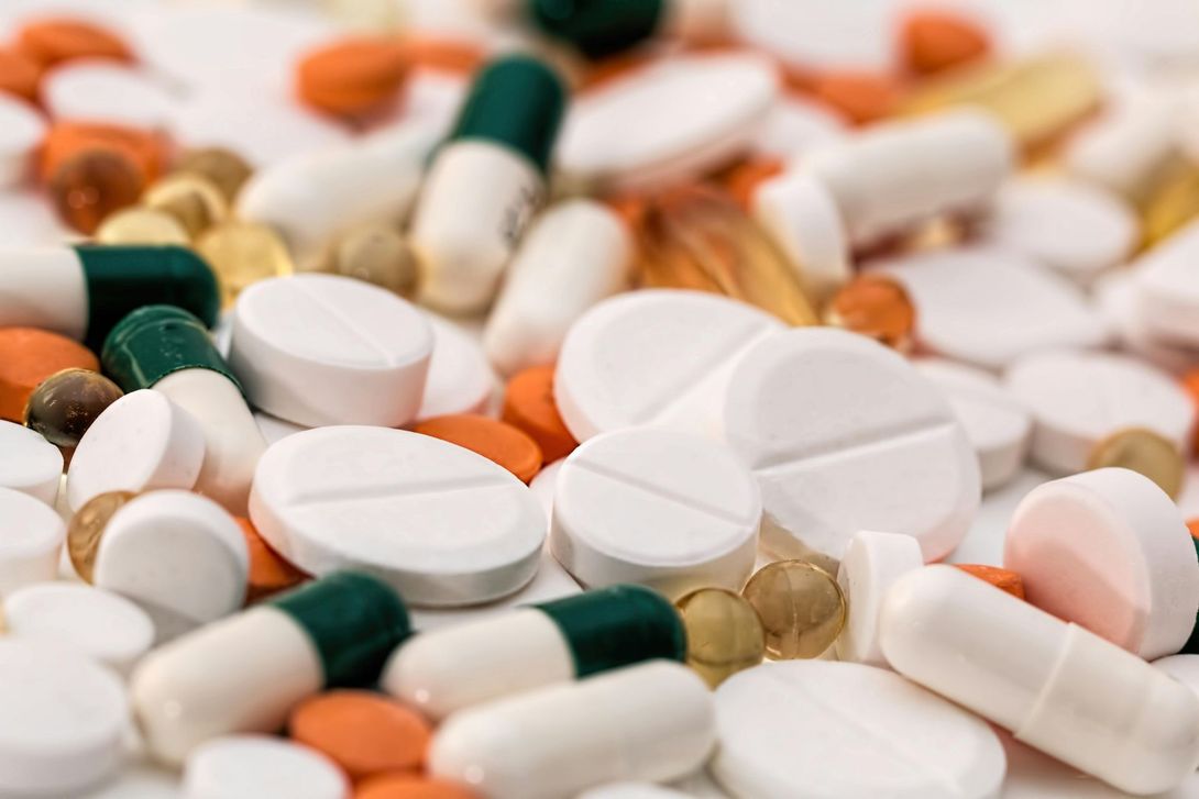 Pills and capsules of various colors scattered on a white surface.