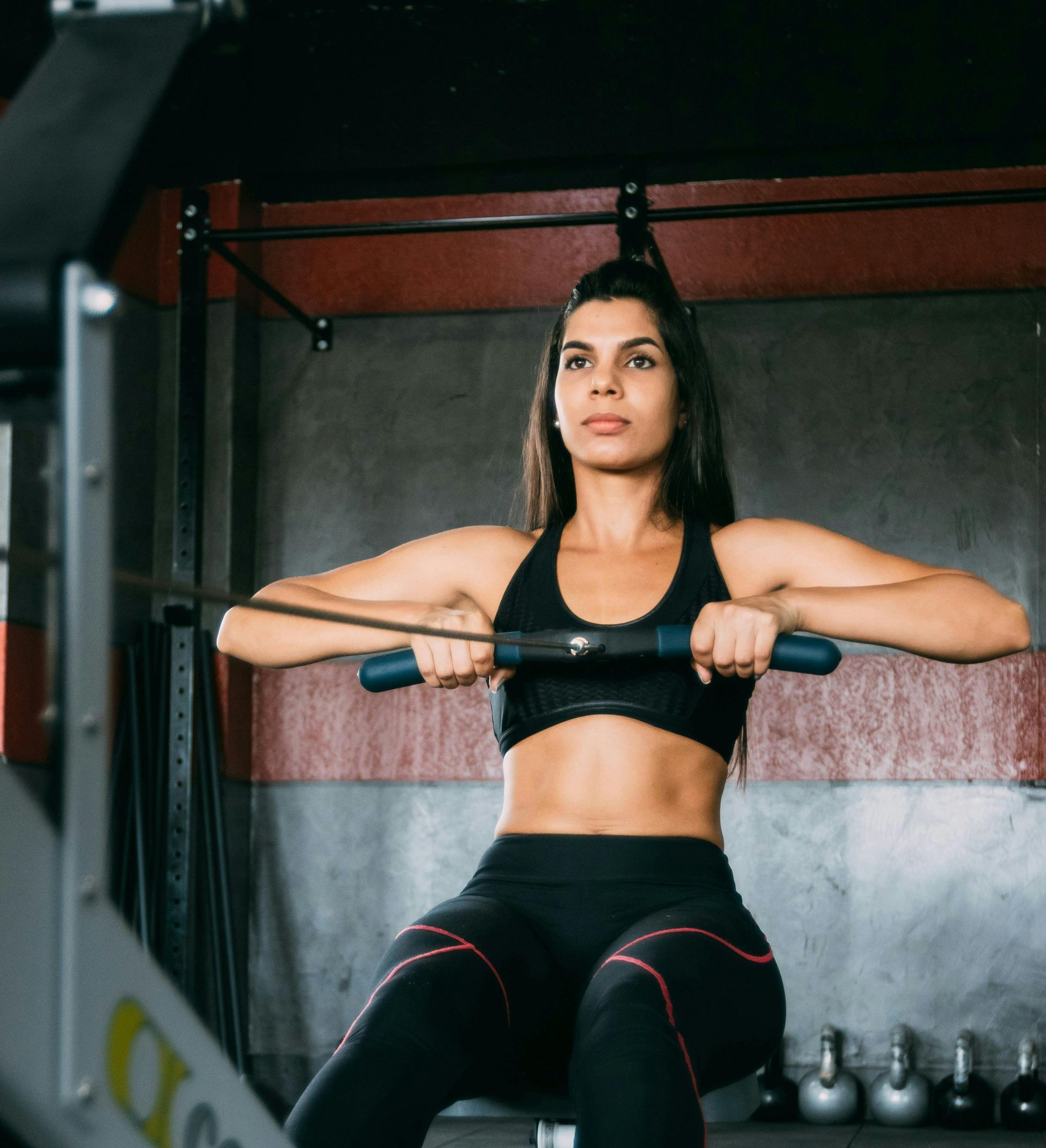 Woman in gym, using rowing machine, wearing black athletic wear, focused expression.