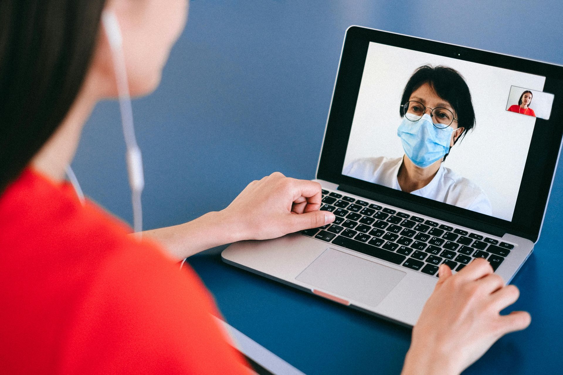 Woman on laptop video call with person wearing a mask, small inset of another person.
