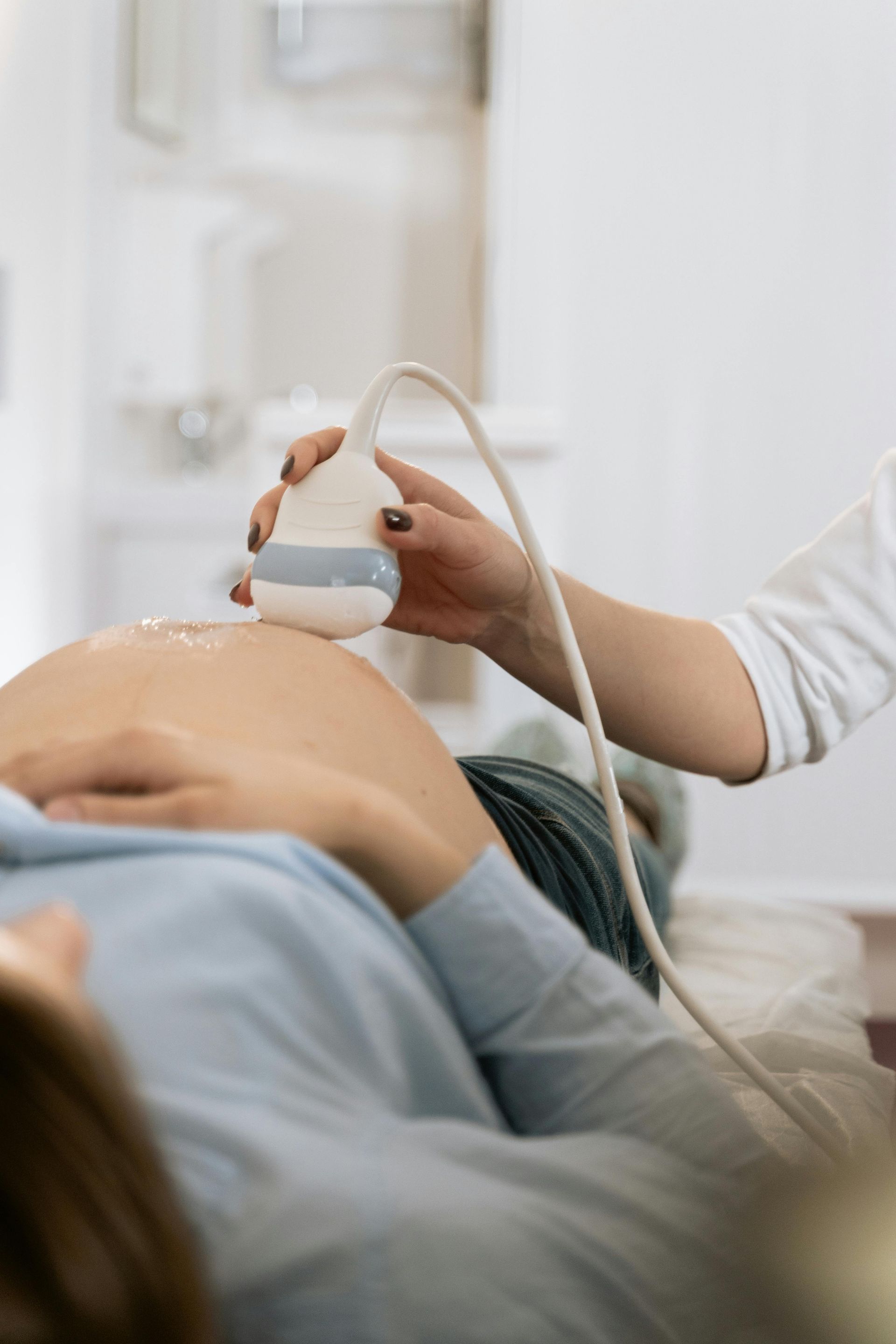 Person giving a pregnant woman an ultrasound scan.  The woman lies on a table in a medical setting.