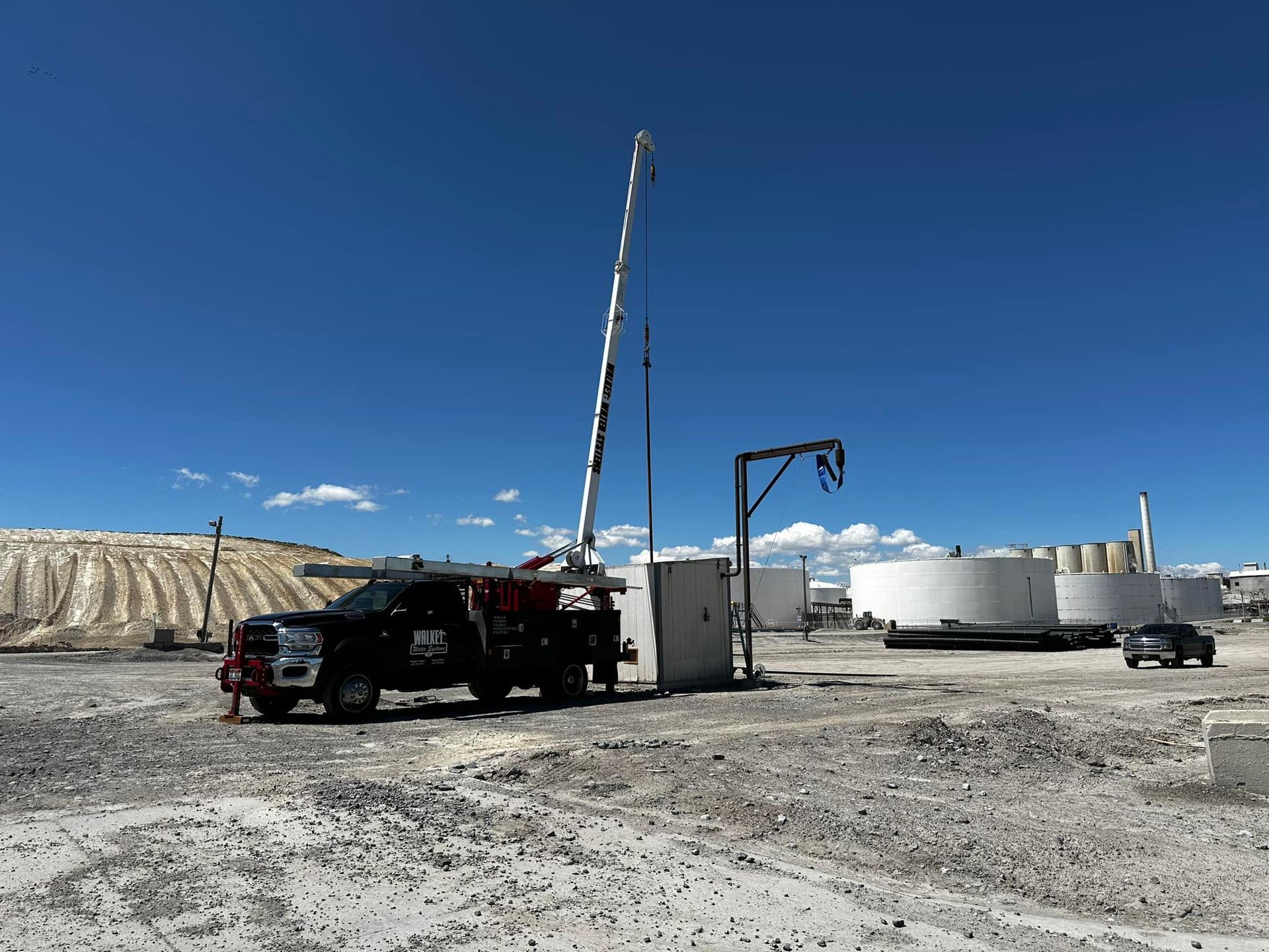 A truck is parked in a dirt field next to a crane.