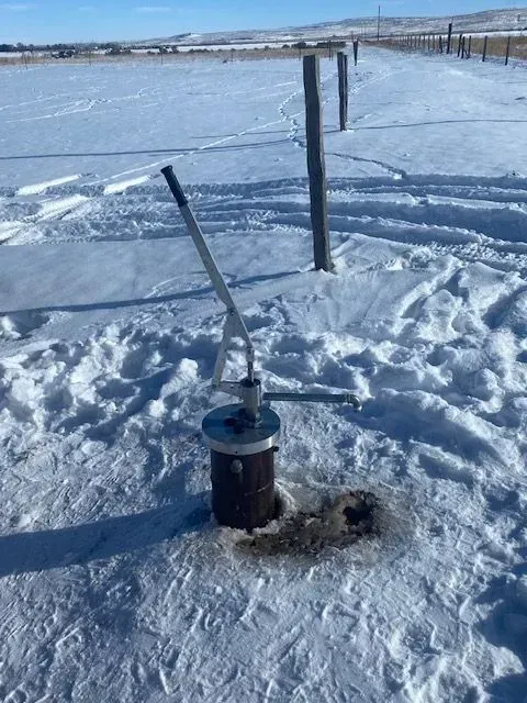 A water pump is sitting in the middle of a snow covered field.
