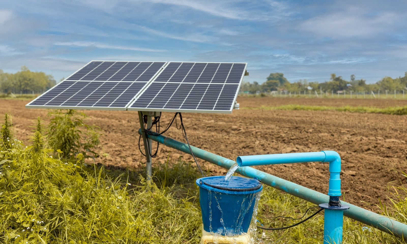 A solar panel is sitting next to a water pump in a field.