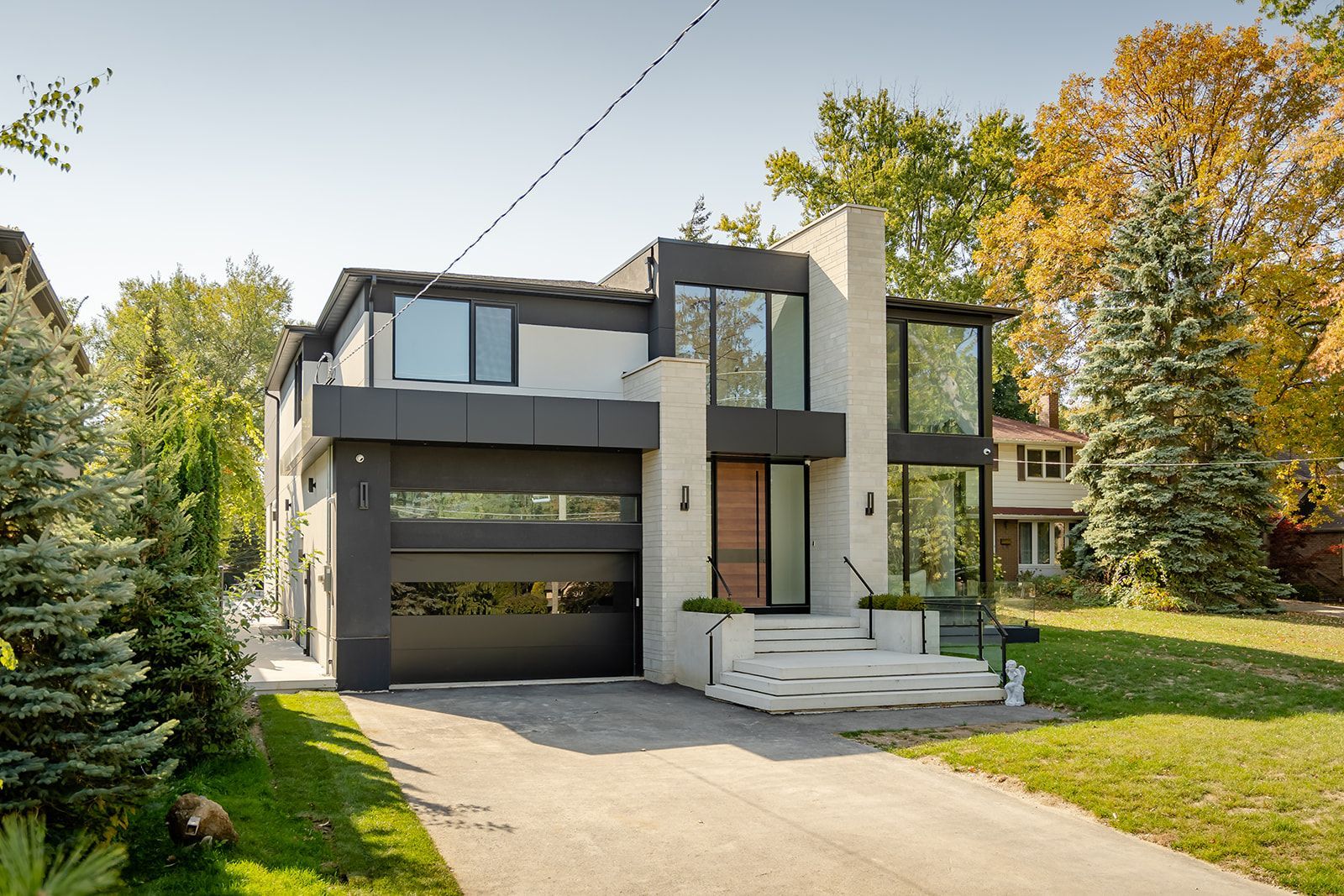 Modern two-story house with dark gray siding, large windows, and a concrete driveway.