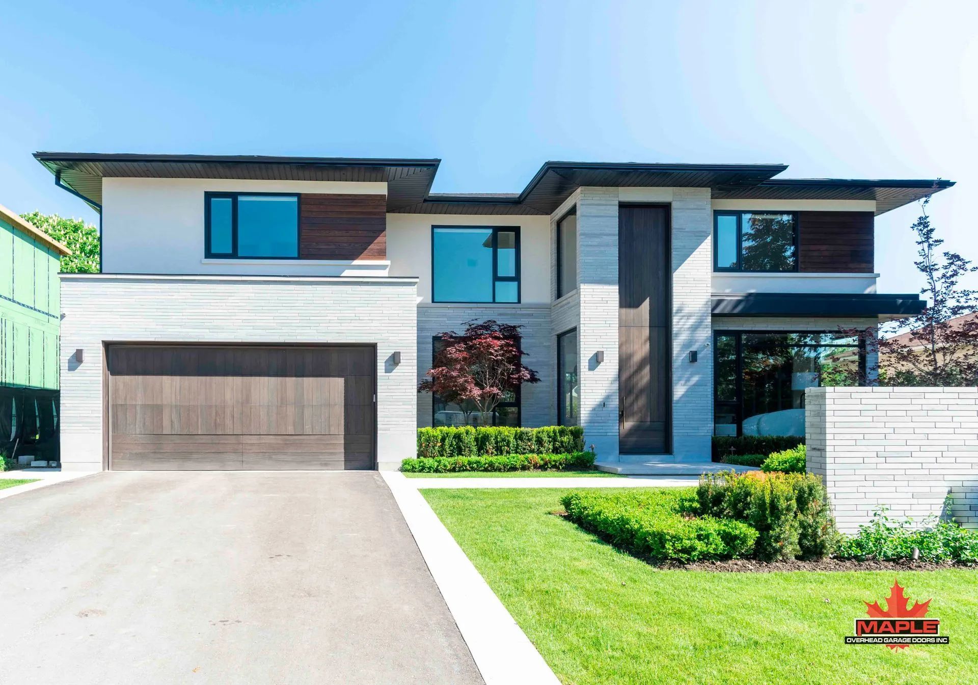 Modern two-story house with garage, large windows, and landscaped front lawn under bright sunlight