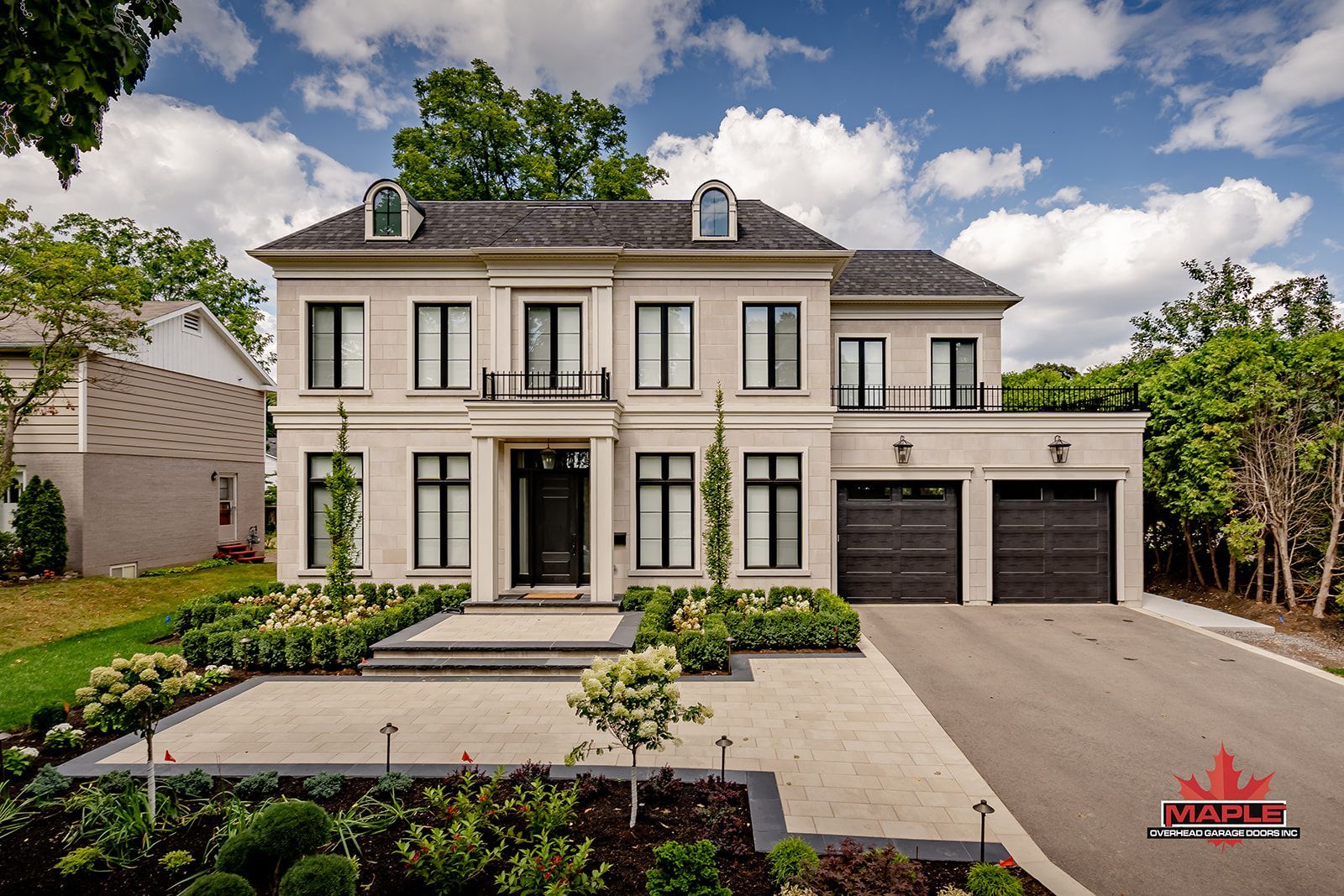 Elegant two-story house with stone facade, black trim, and a three-car garage; landscaped front yard with a paved driveway.