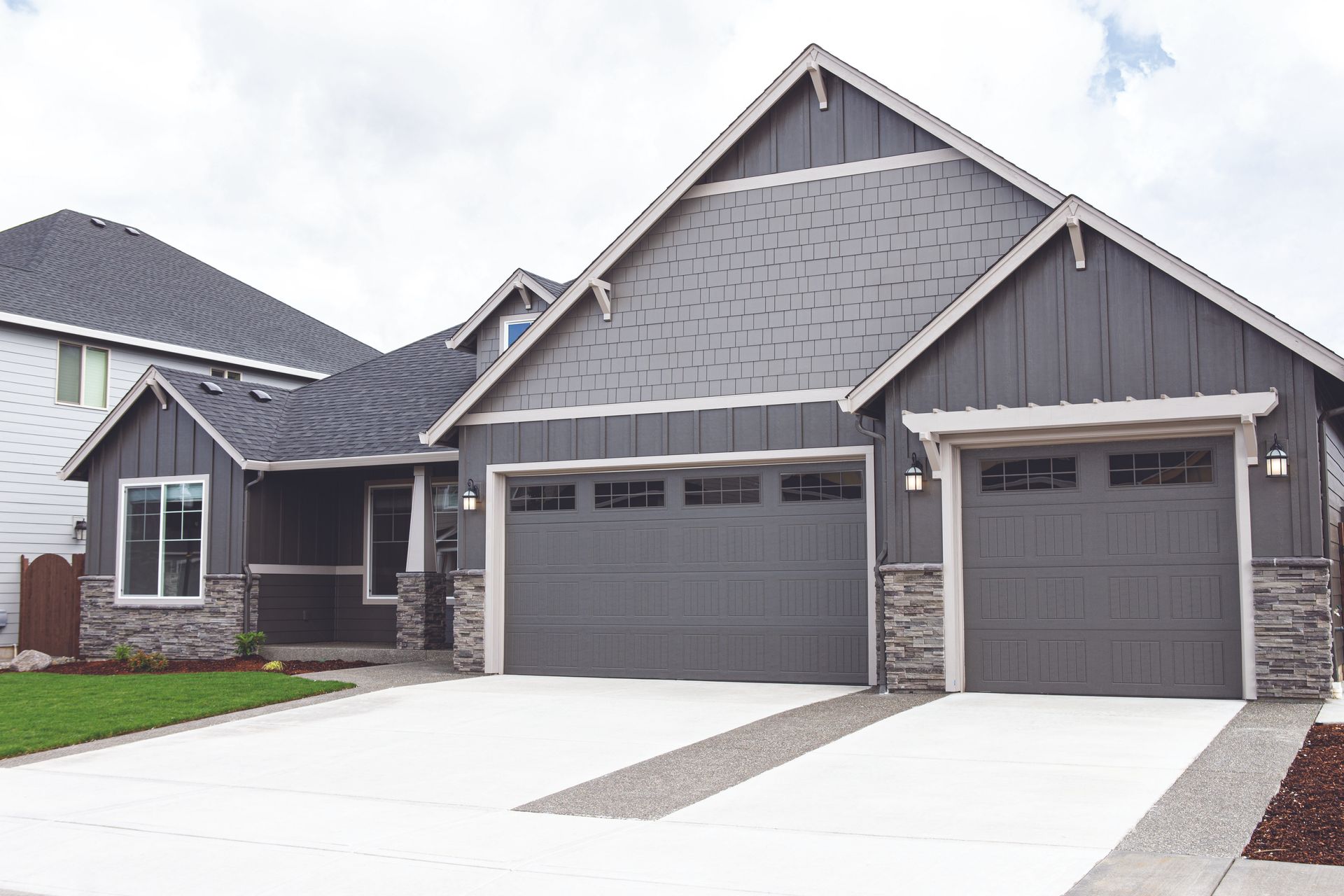 Modern gray house with two garages, stone accents, and a white driveway