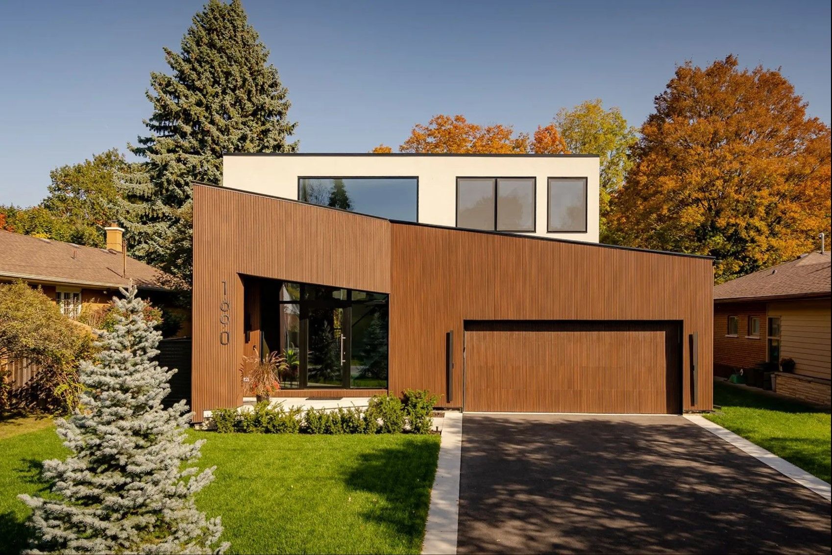 A modern house with a wooden garage door is surrounded by trees