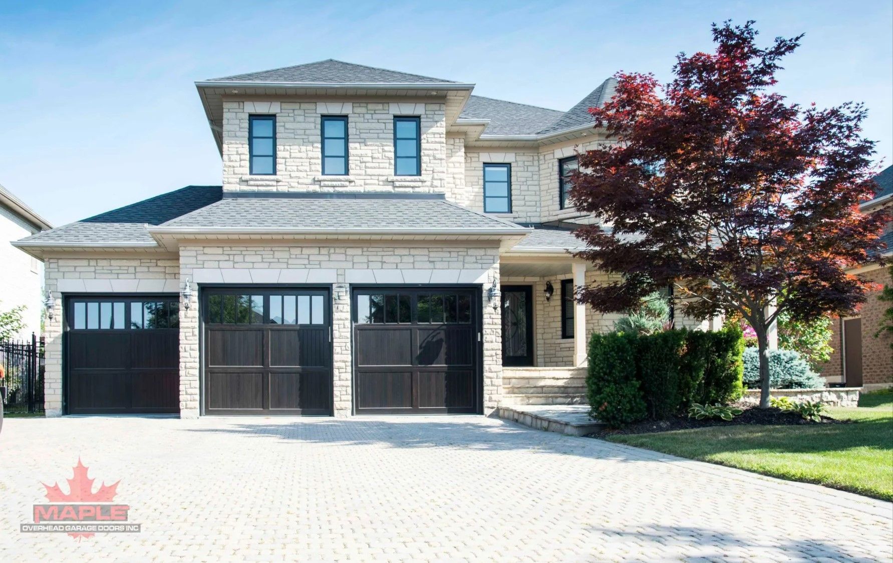 A large brick house with black garage doors and a tree in front of it