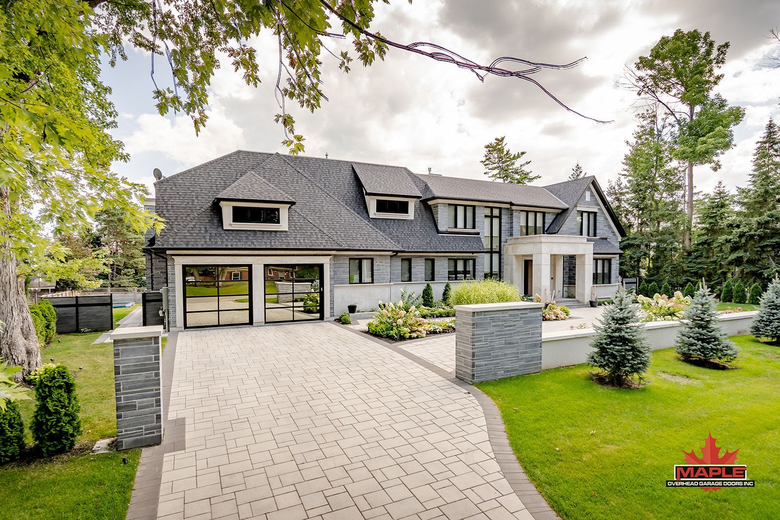 Two-story modern home with gray roof, brick driveway, and manicured lawn.