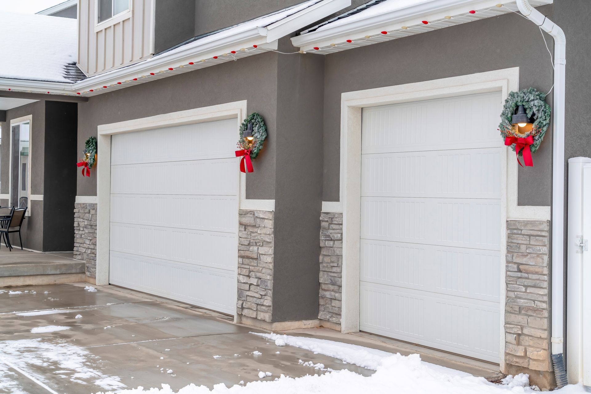 Two white garage doors with wreaths, snow on the driveway.