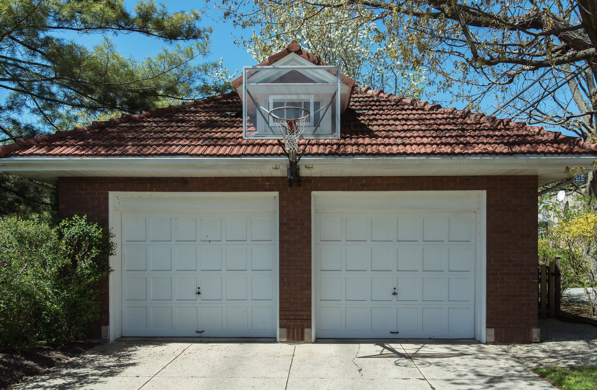 A brick garage with two white garage doors and a red roof