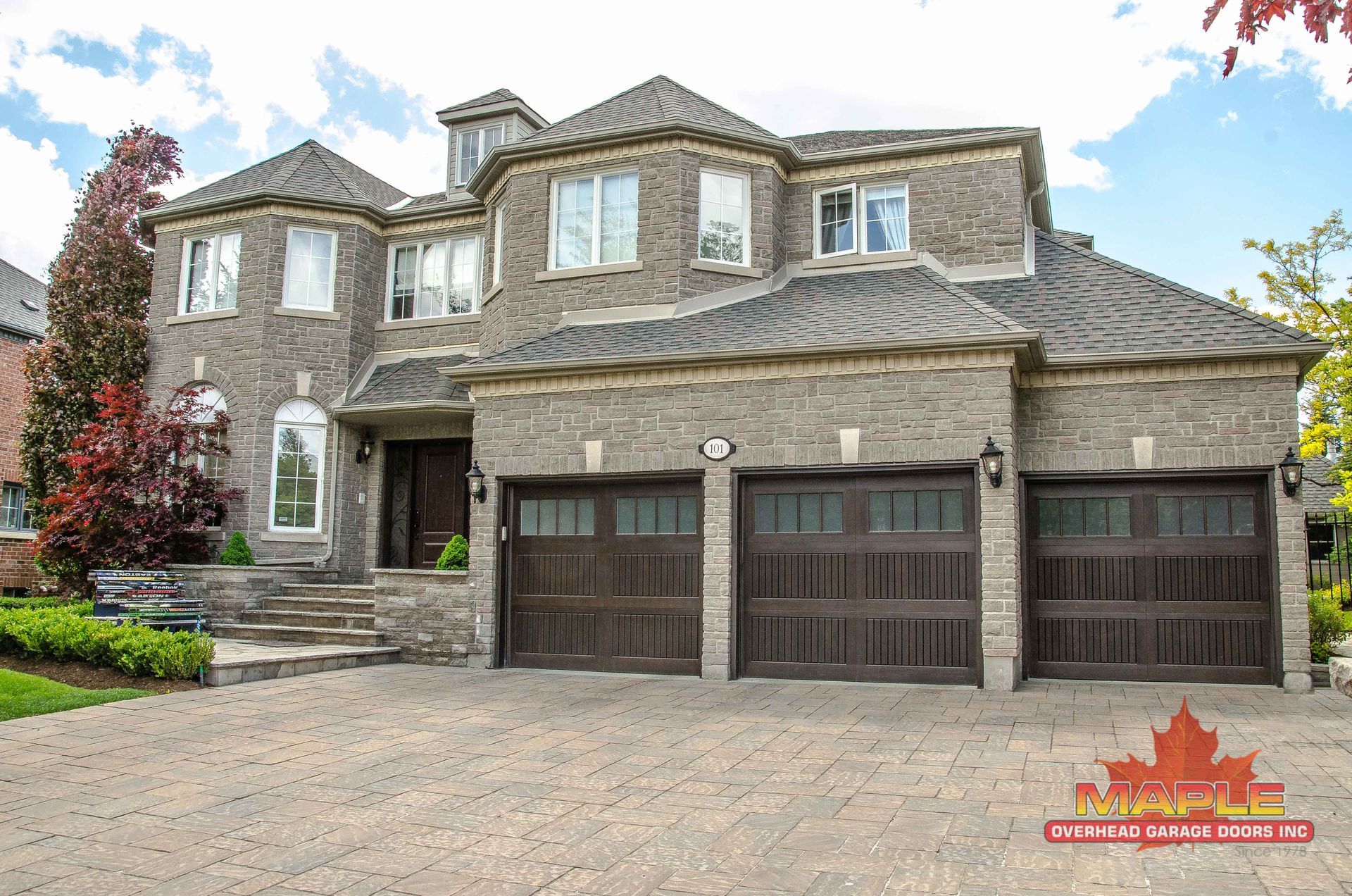 A large brick house with three garage doors and a large driveway.