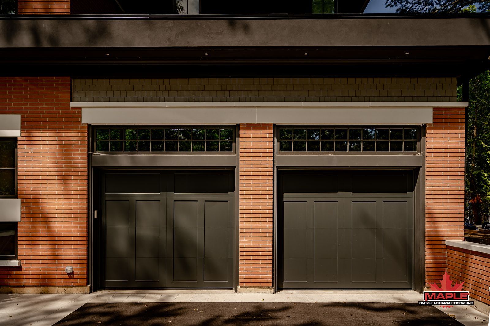 Two dark gray garage doors with small windows above, in a brick building.