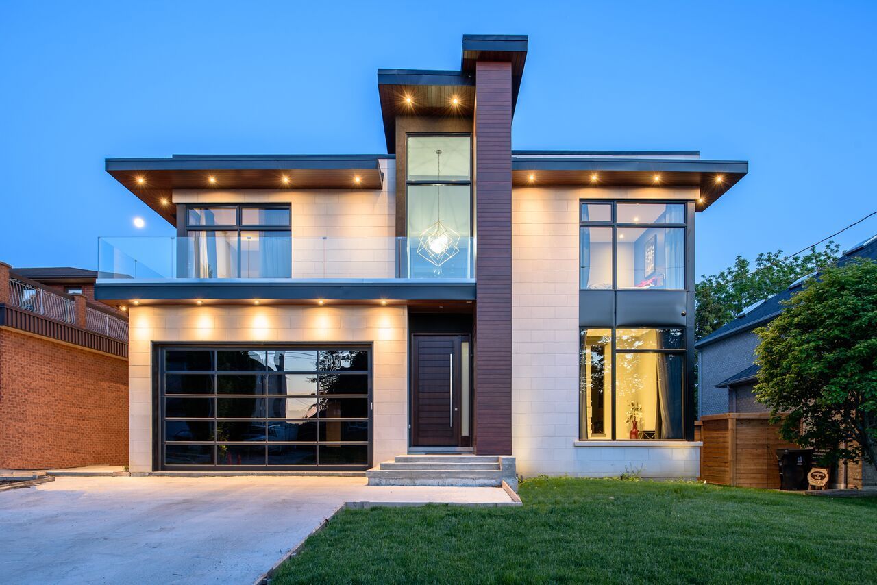 A modern house with a large garage and a lot of windows is lit up at night.