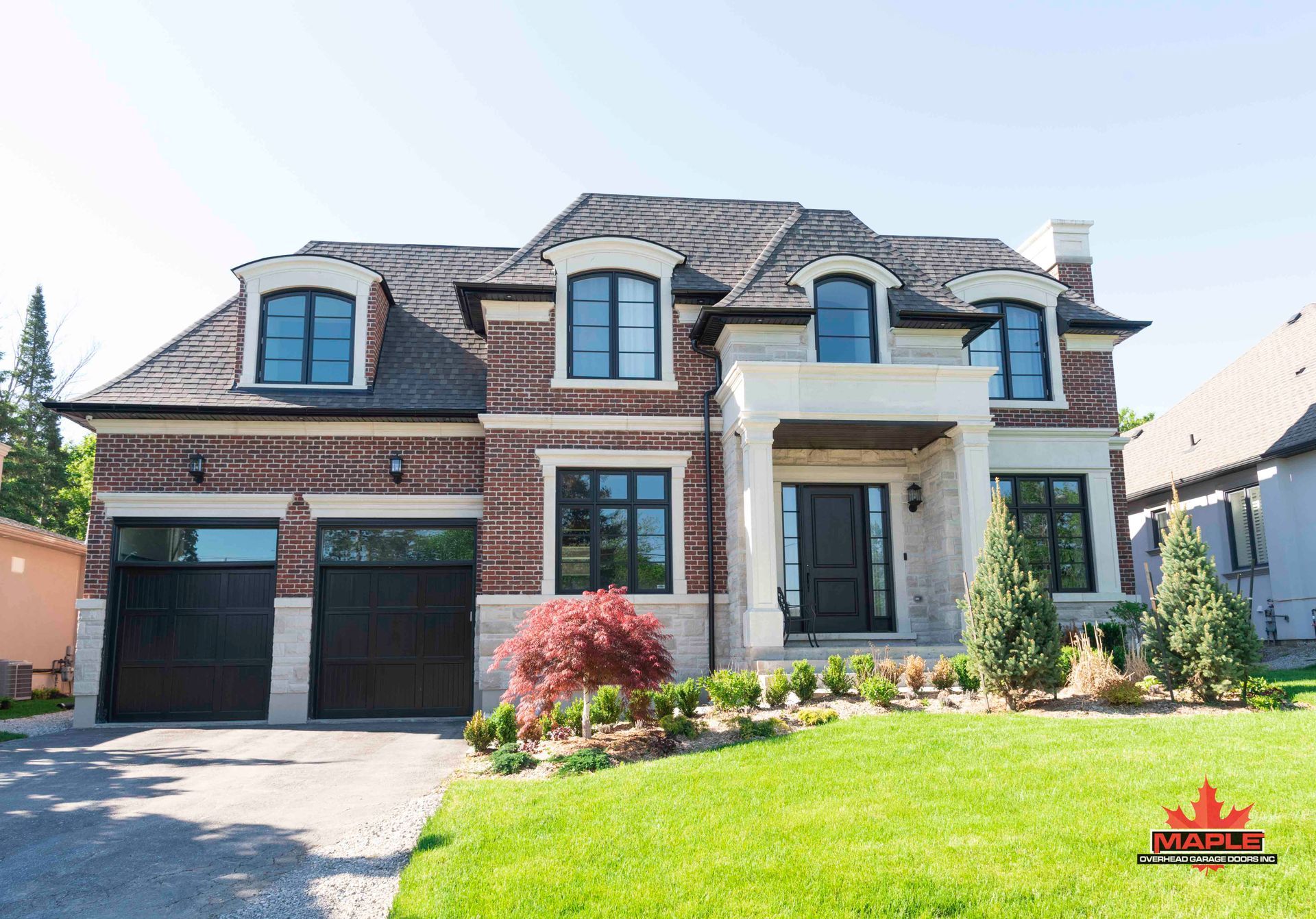 A large brick house with two garages and a large lawn in front of it.