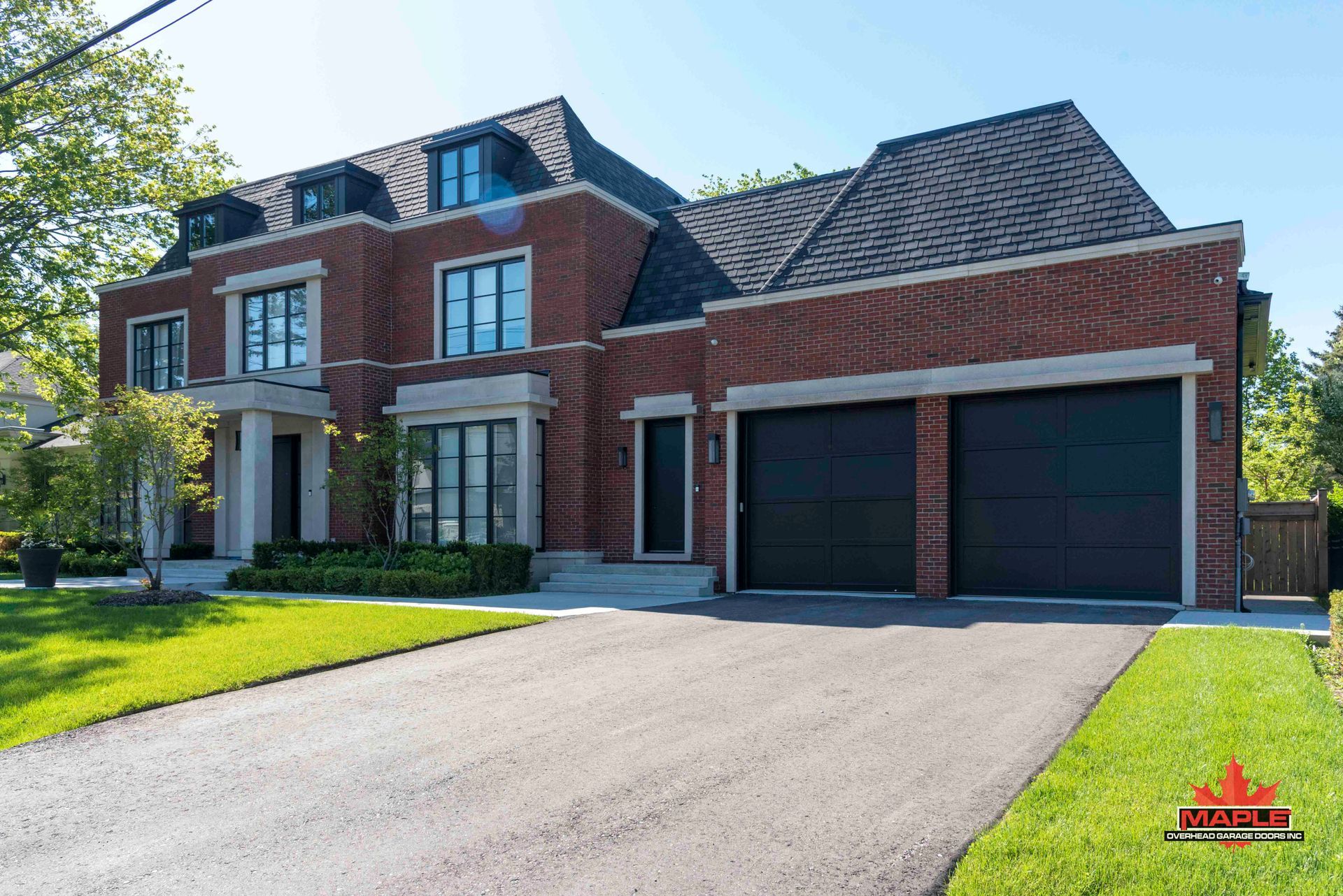 A large brick house with two black garage doors and a driveway.
