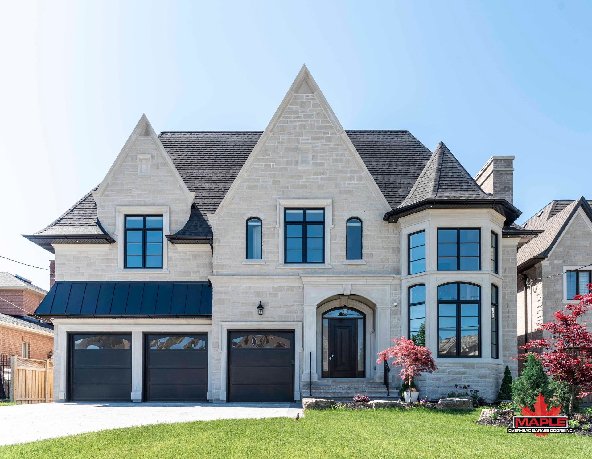 A large house with a lot of windows and a black roof is sitting on top of a lush green lawn.