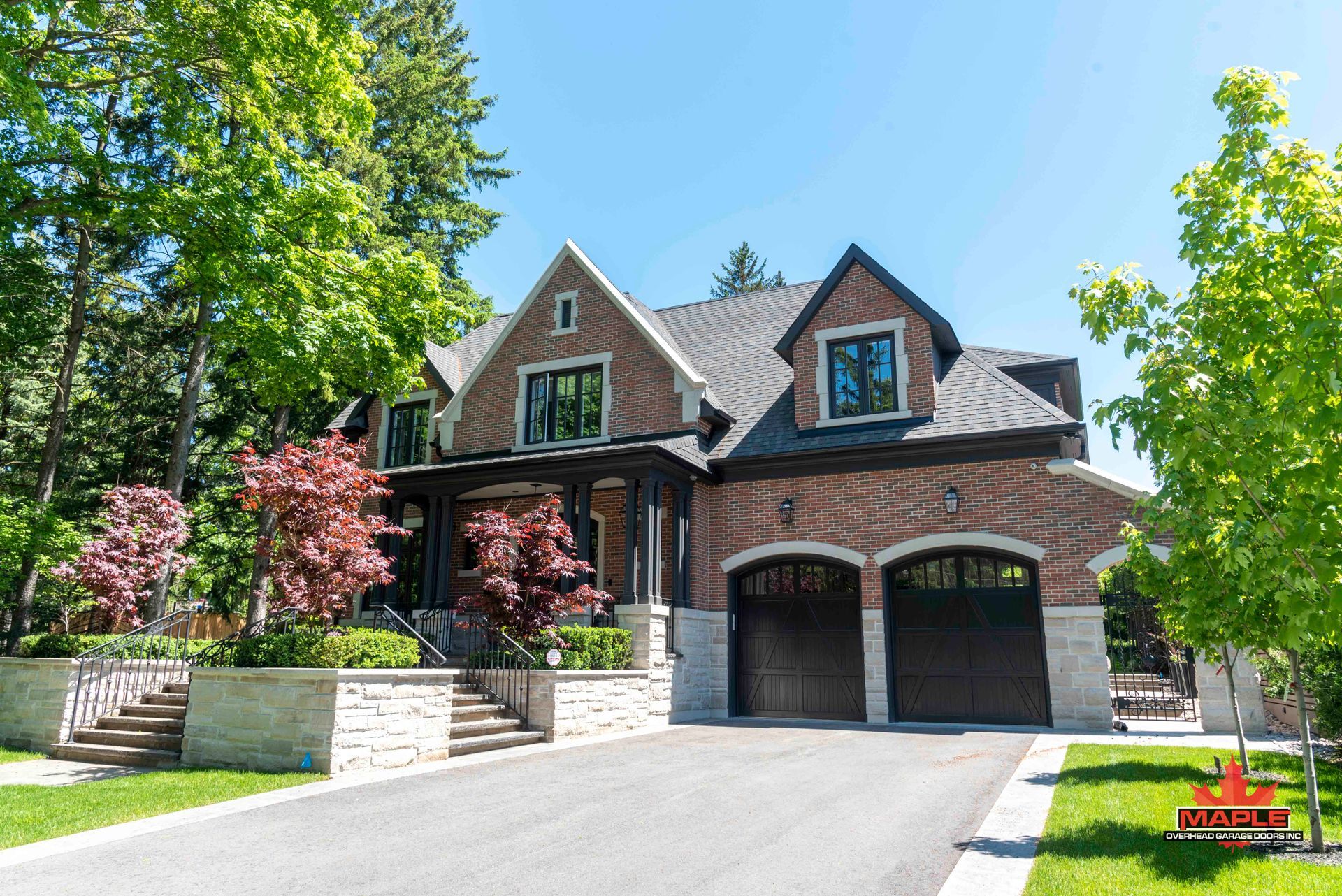 A large brick house with two garages is sitting on top of a lush green hillside.
