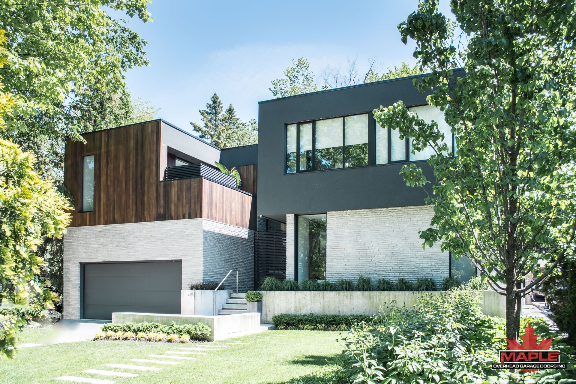 A modern house with a large garage is surrounded by trees.