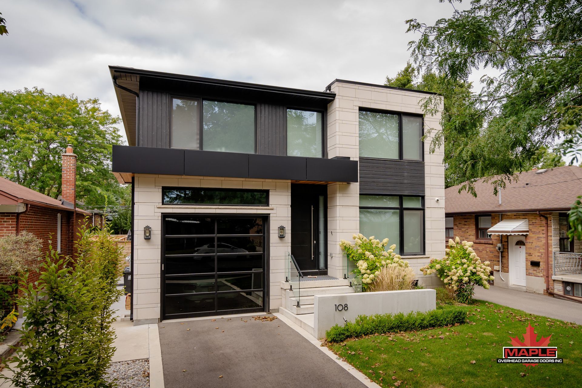 A modern house with a black garage door and a brick house in the background.