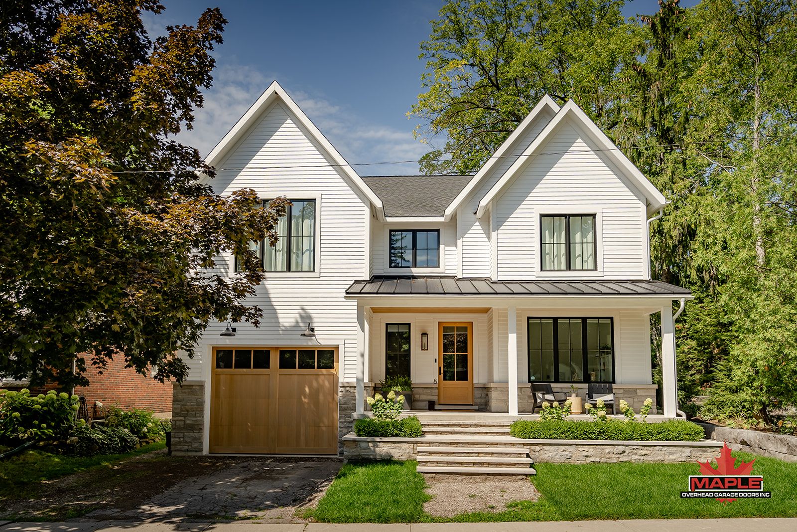 A white house with a wooden garage door is surrounded by trees.