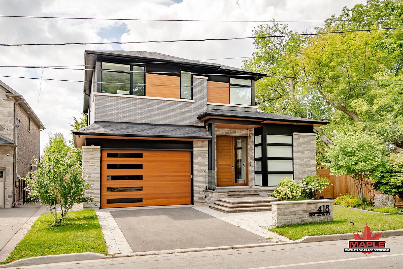 A modern house with a wooden garage door is sitting on the corner of a street.