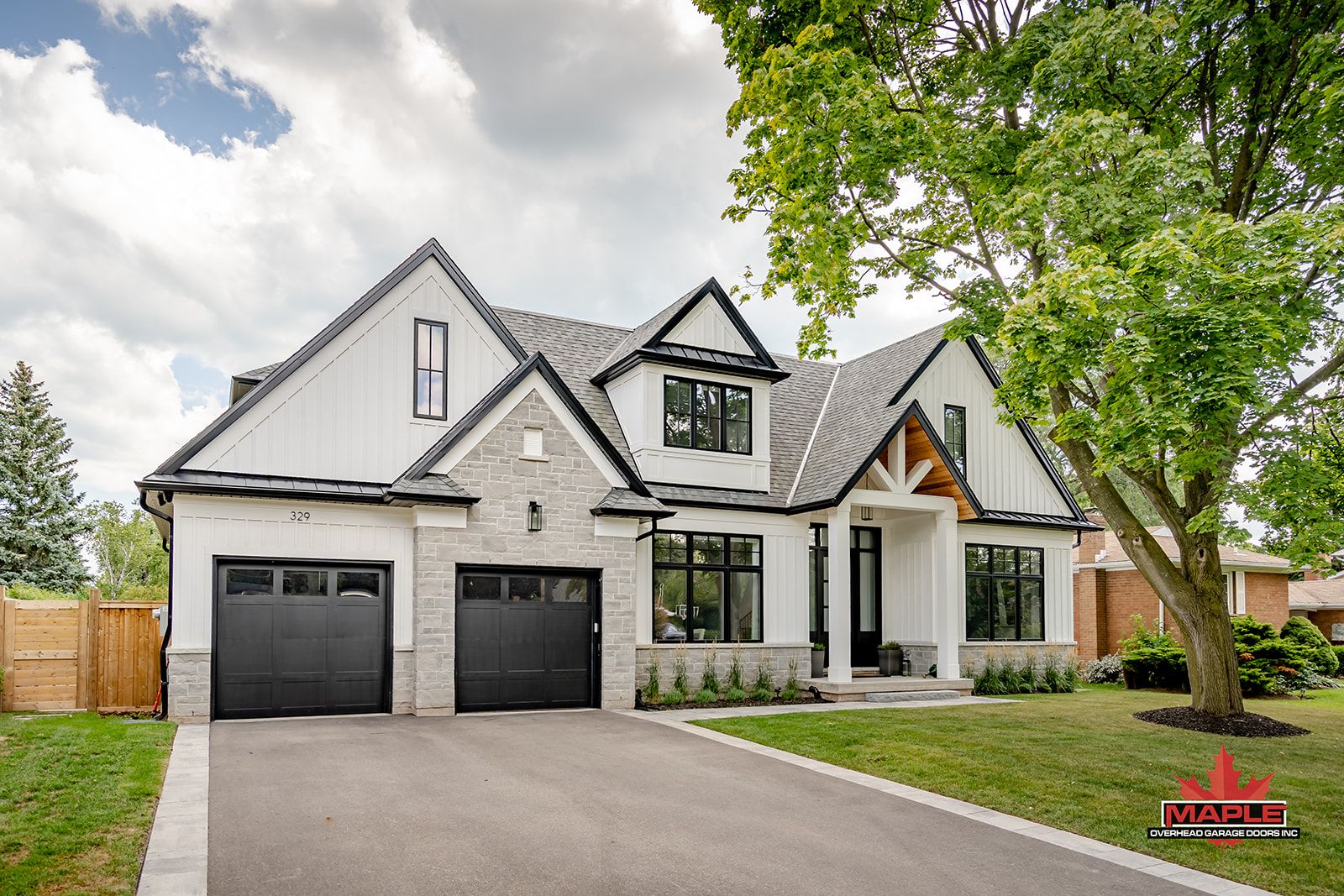 A large white house with two black garage doors and a tree in front of it.