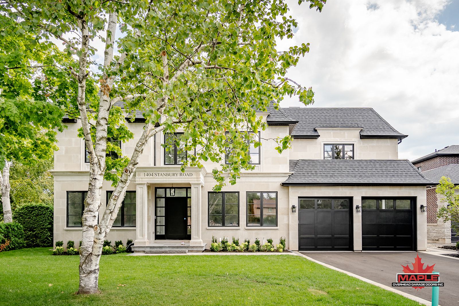 A large white house with black garage doors and a tree in front of it.
